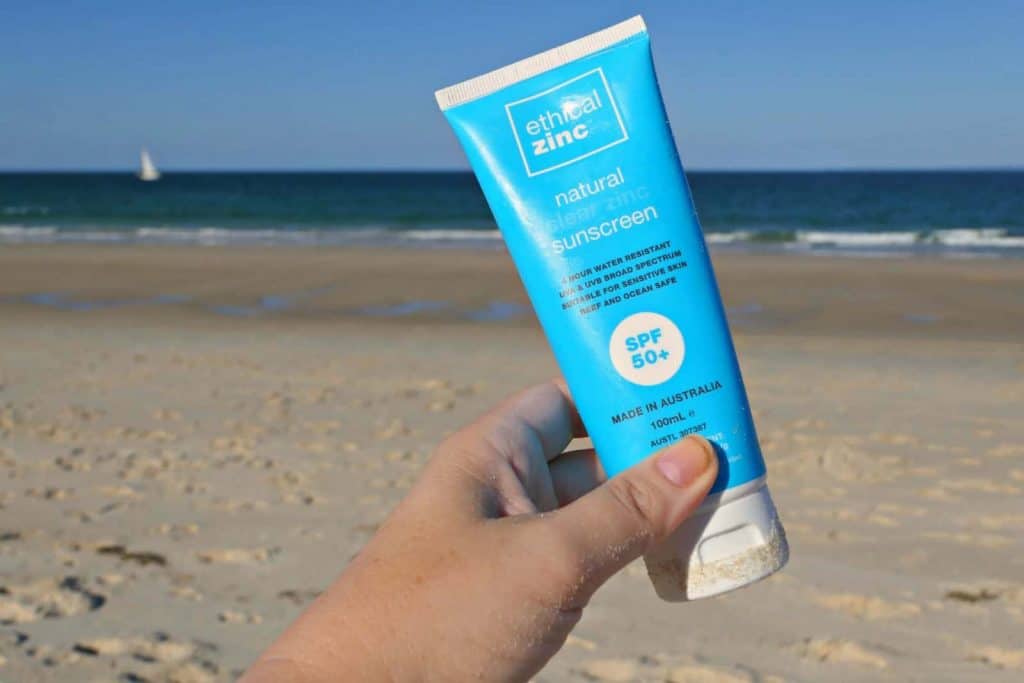 Bottles of Ethical Zinc sunscreen being held over a beach