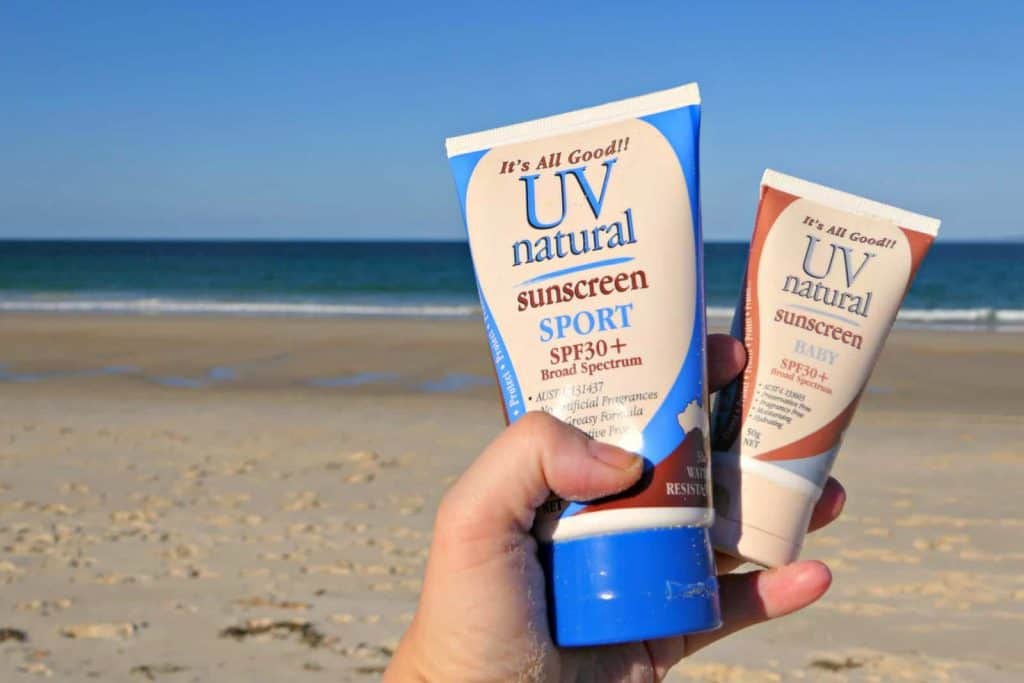 Bottles of UV Natural zinc sunscreen being held over a beach