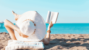 A lady laying on the beach reading a book