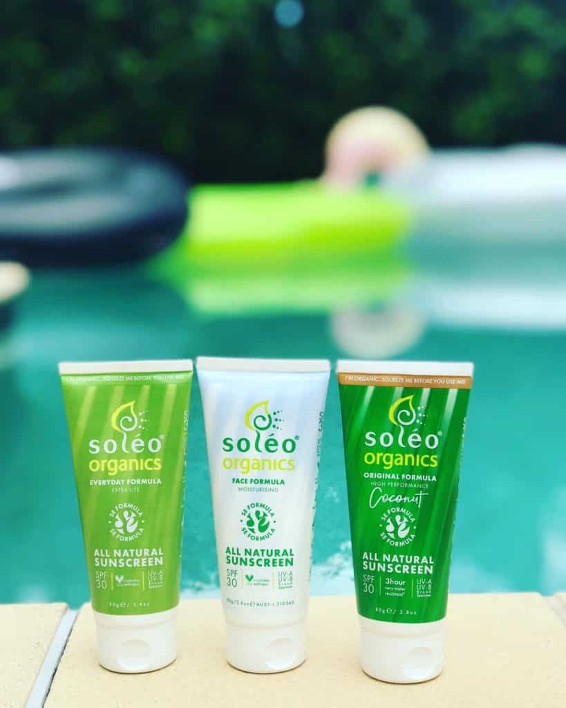 Three bottles of Soleo Organics sunscreen beside a pool
