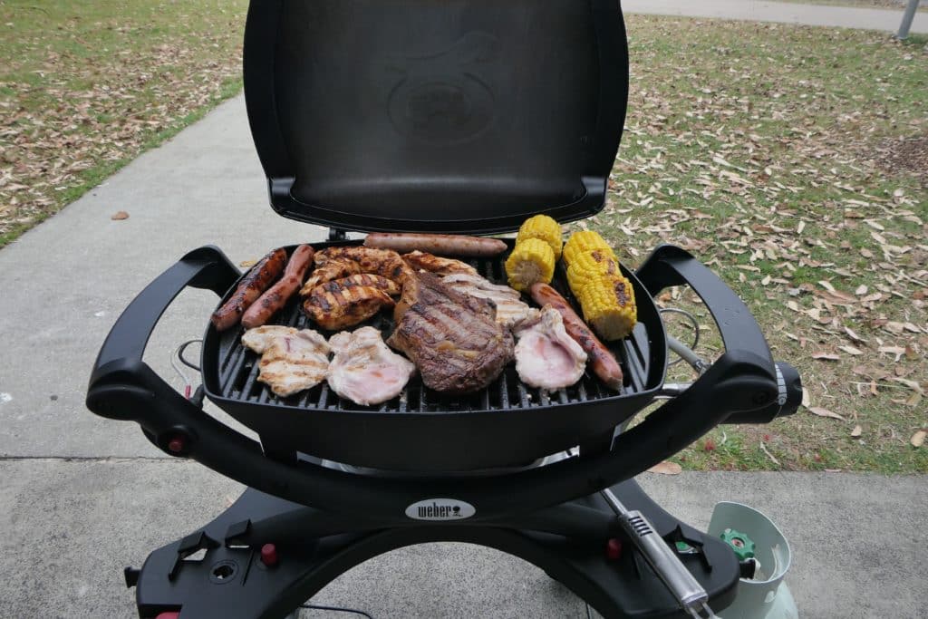 A Weber Baby Q BBQ with food on the grill